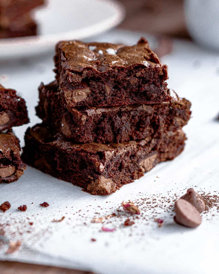 Brownies squares cut and stacked on top of each other. With a few chocolate chips laying next to them.