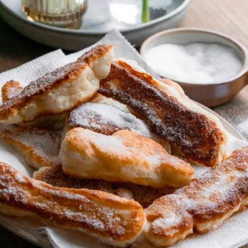 Fried pizza dough strips on a plate covered in white sugar