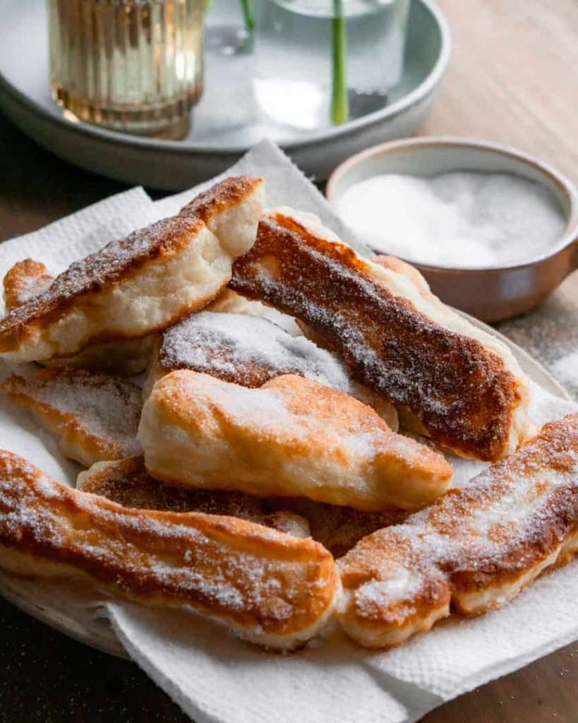 Fried pizza dough strips on a plate covered in white sugar
