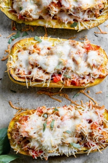 Delicata Squash cut in half on a baking sheet. It has been stuffed with veggies and ground beef and topped with melted mozzarella cheese.
