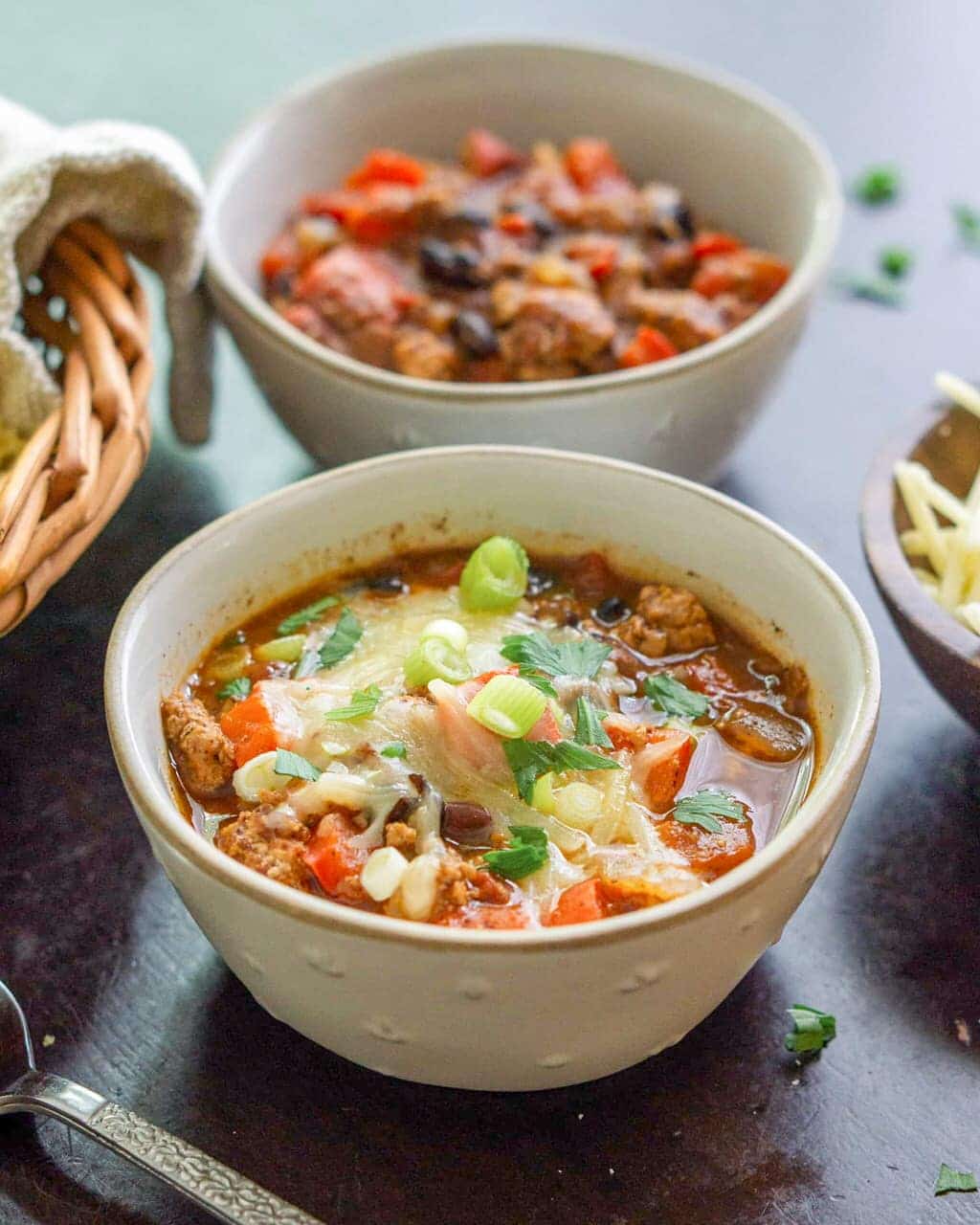 Two bowls of chili with shredded cheese and green onions on top of them