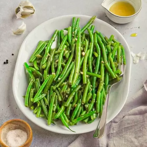 Green beans on a platter with a small pitcher of olive oil, garlic clove and small bowl of salt next to it.