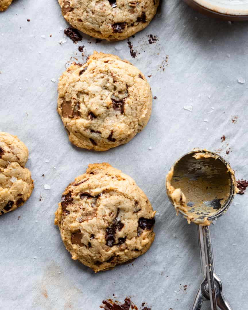 Baked chocolate chip cookies with a cookie scoop laying next to them.