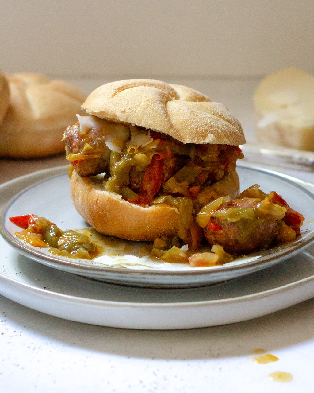 Italian Sausage & Peppers sandwich on a plate. There is some spilled over sausage bites and peppers next to the sandwich on the plate.