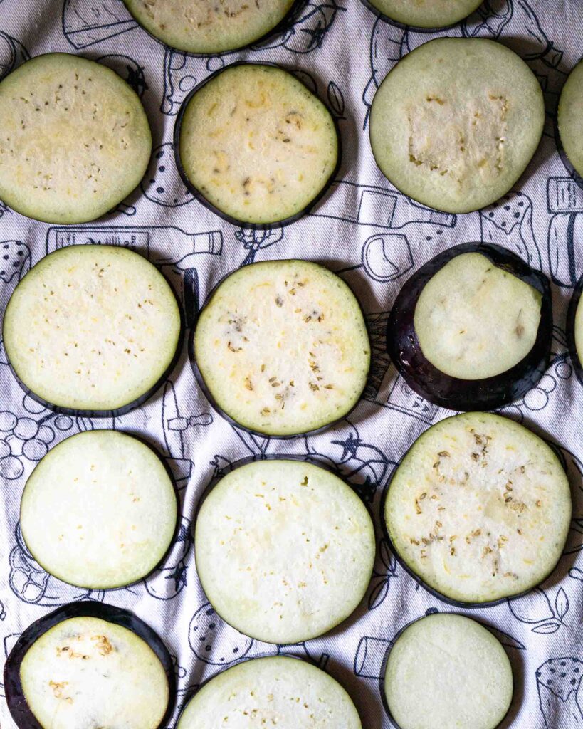Sliced eggplant rounds on a tea towel drying.