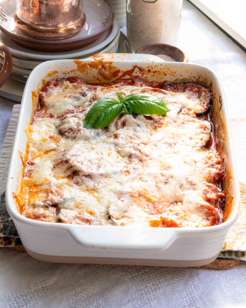 Baked eggplant parmesan with a sprig of basil leaves.