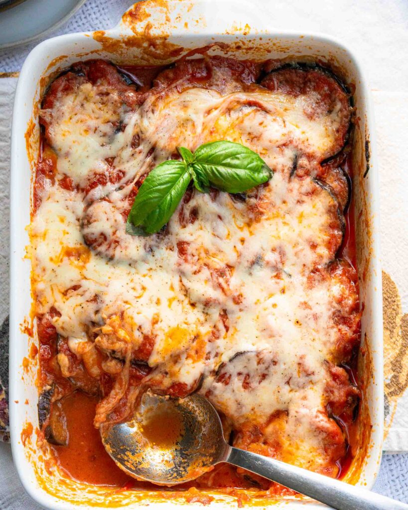 A baking pan of eggplant parmesan with a scoop missing and a spoon sitting in the pan.