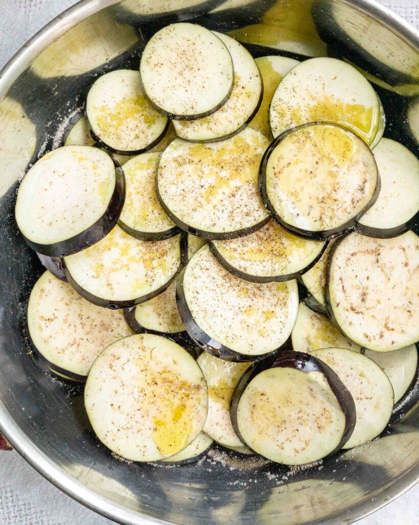 Eggplant rounds drizzled with olive oil, salt and pepper in a large bowl.