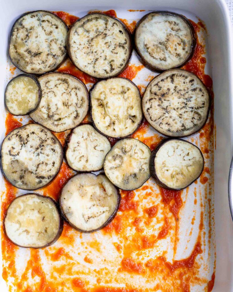 Eggplant rounds on top of a thin layer of sauce in a baking pan.