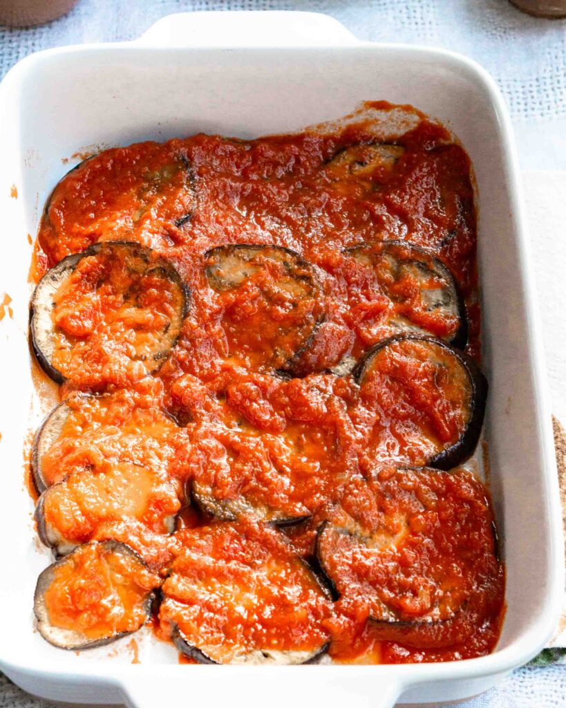 Eggplant rounds in a baking pan covered in sauce.