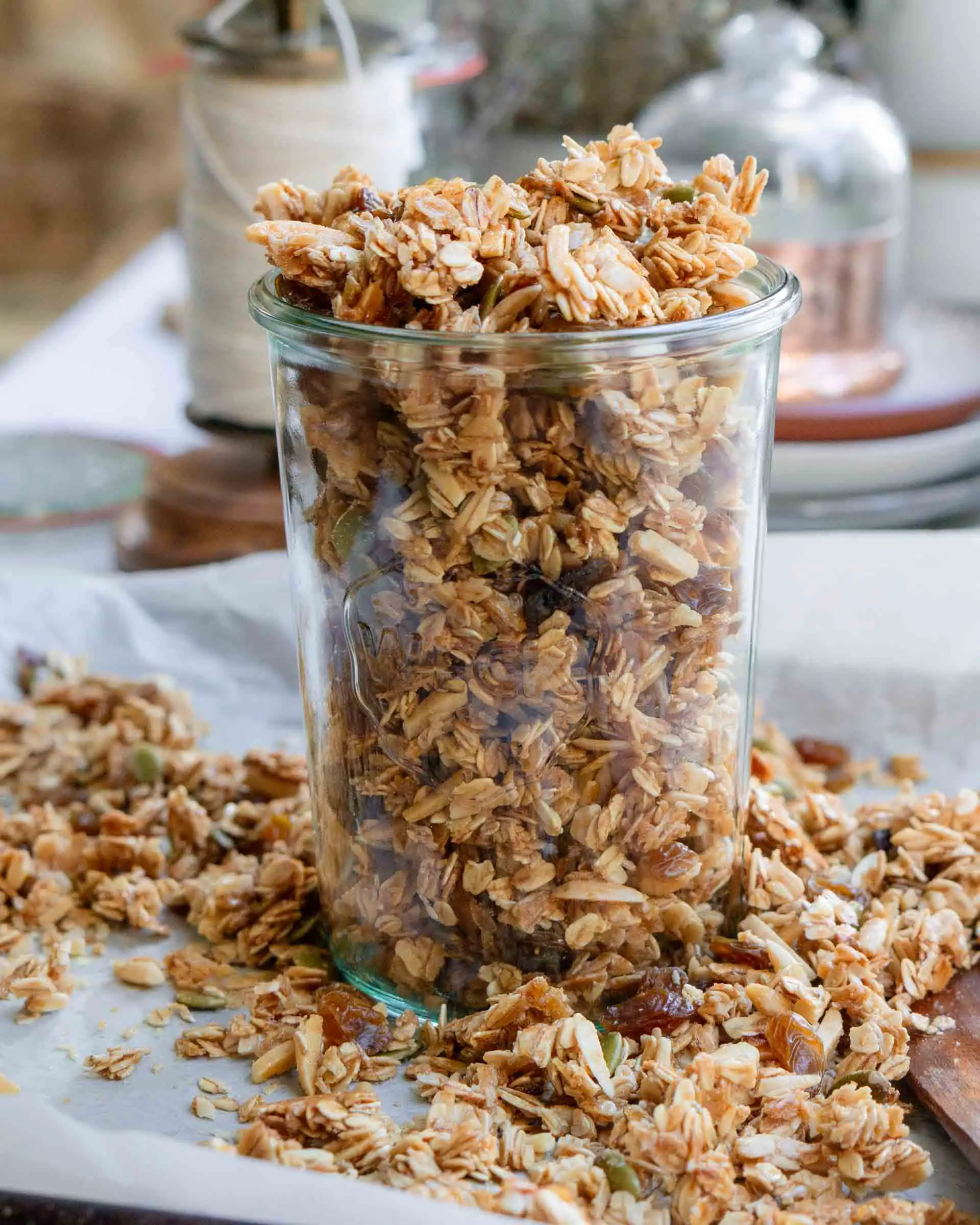 Honey almond granola in a large glass jar. The jar is sitting on a baking sheet and is surrounded by granola.