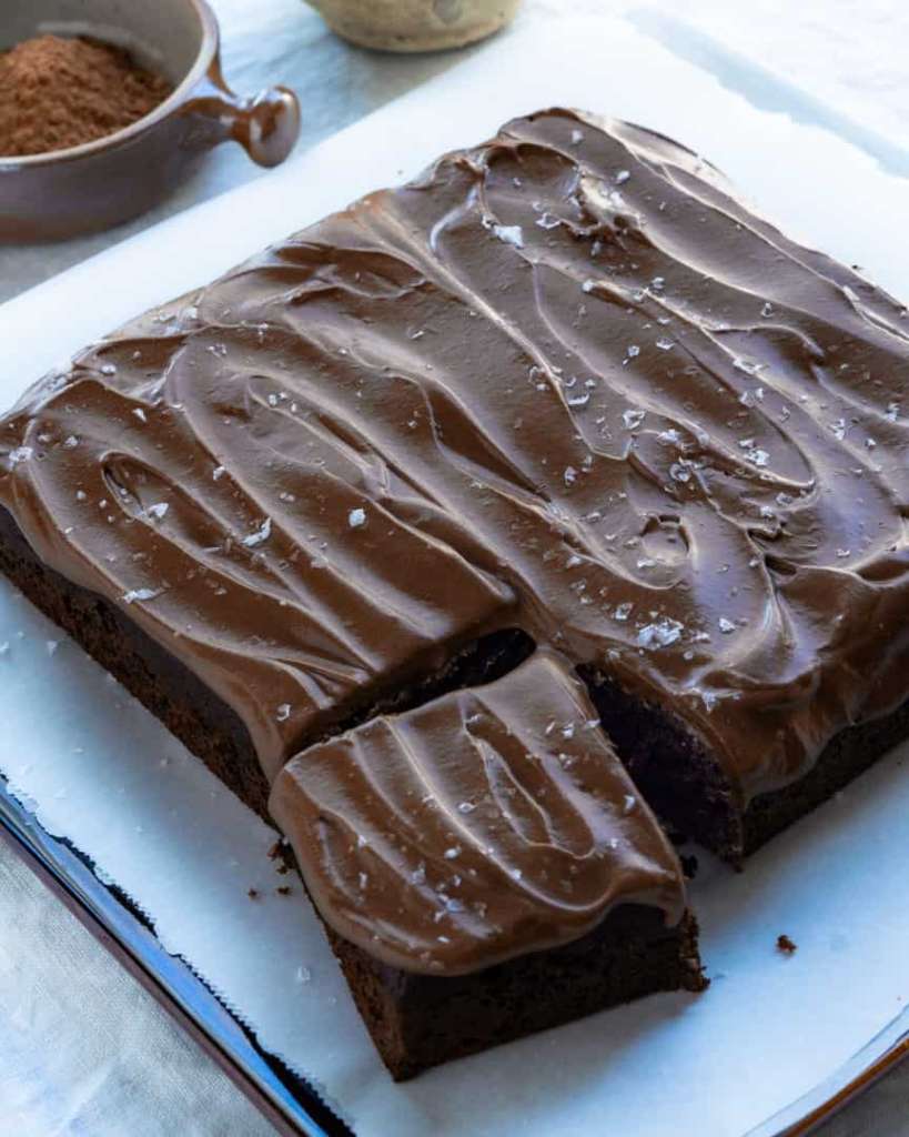 One layer chocolate cake that is in a square shape with one piece cut and slightly pulled away from the rest of the cake. The top the cake is frosted with chocolate frosting and sprinkled with large sea salt flakes.