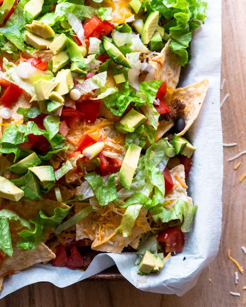 Nachos on a baking sheet with lettuce, tomatoes, cheese, avocado's on top