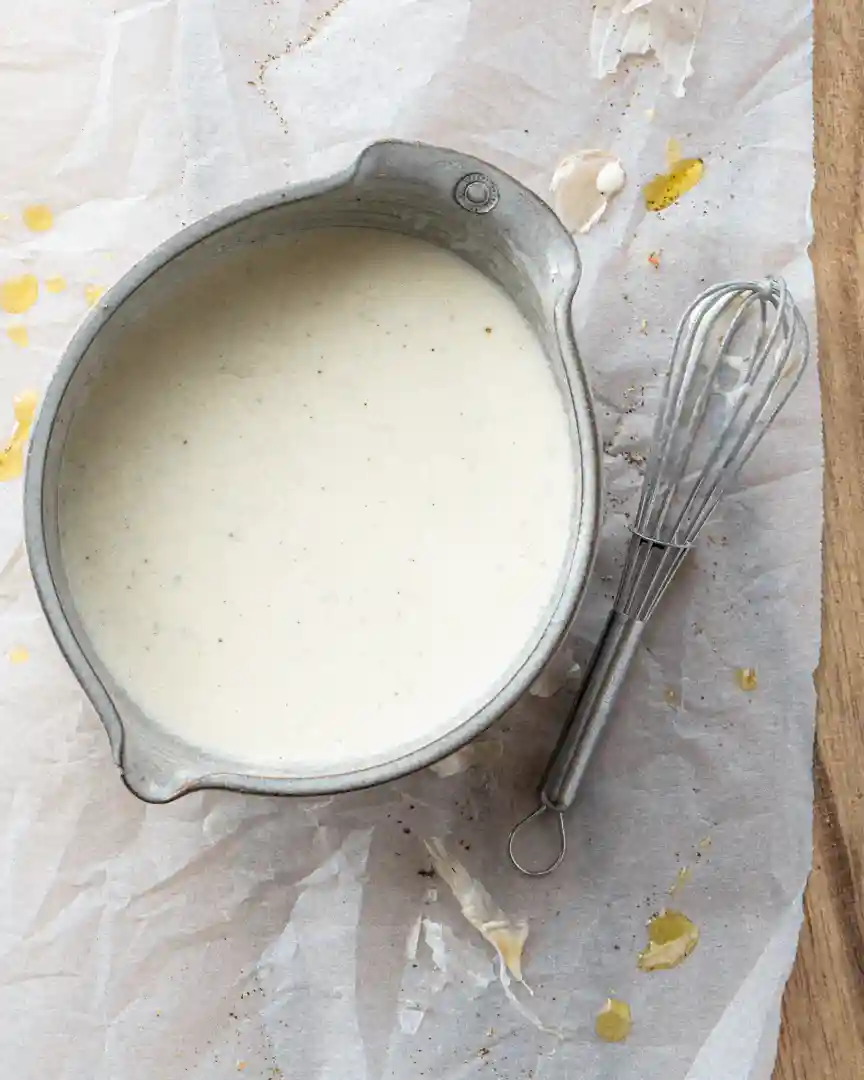 Bowl of creamy lemon dressing with whisk next to it.