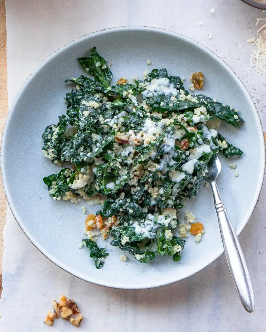 Kale and quinoa salad with a fork and golden raisins scattered on the plate
