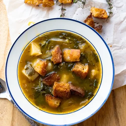 Bowl of Caldo Verde Soup with croutons on top and scattered on side of bowl