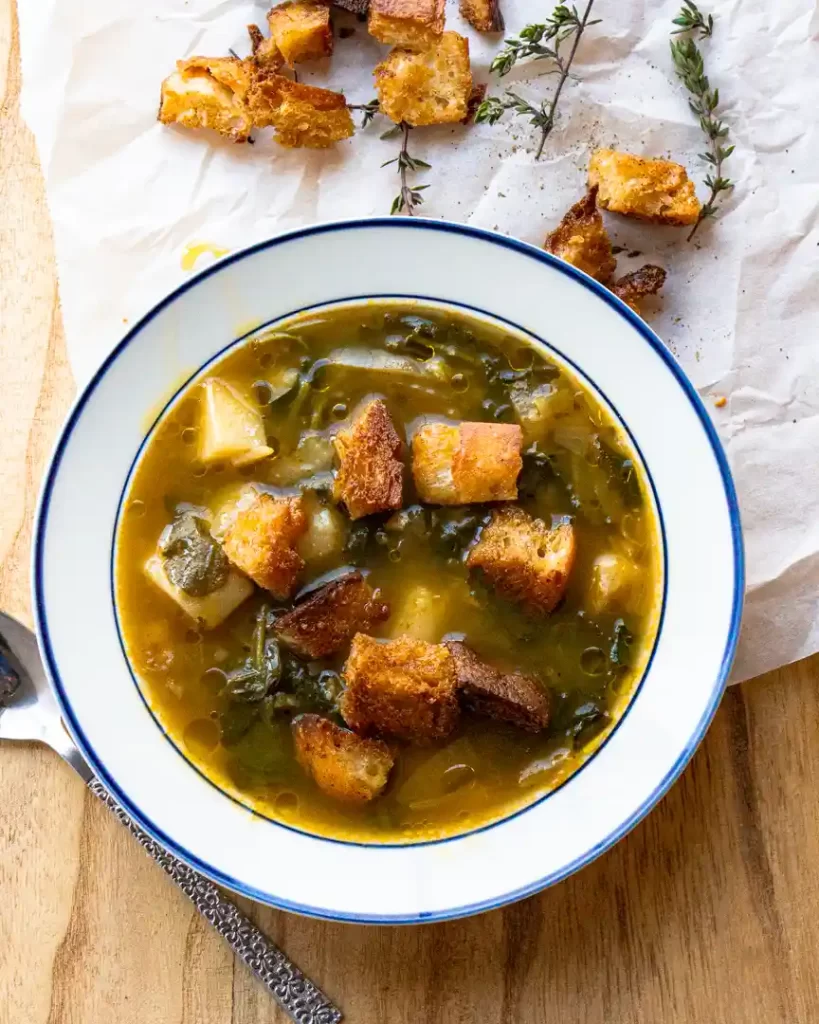 Bowl of Caldo Verde Soup with croutons on top and scattered on side of bowl
