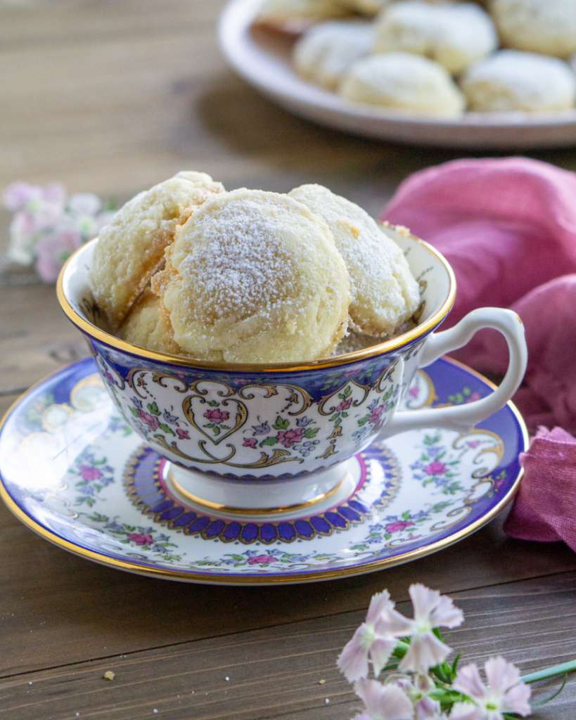 Gluten-free lemon butter cookies sitting in a tea cup. The tea cup is on a small saucer.
