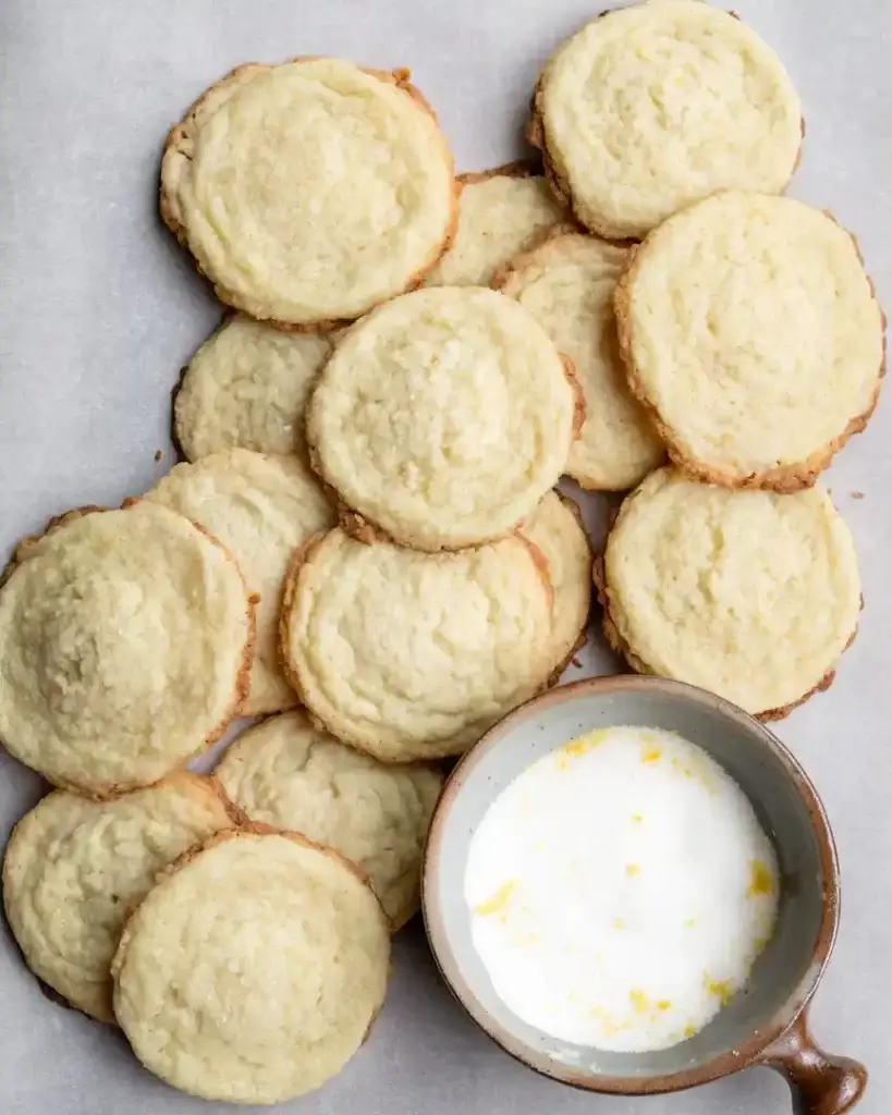 Cookies piled high with a small bowl of lemon sugar next to them