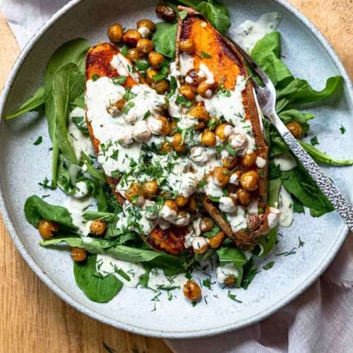 Sweet potato cut in half on a bed of lettuce and topped with chickpeas, dressing, and herbs