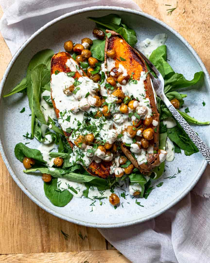 Sweet potato cut in half on a bed of lettuce and topped with chickpeas, dressing, and herbs