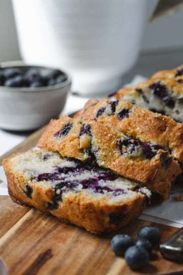 Blueberry loaf cake sliced with slices layered onto of each other. A bowl of blueberries next to it.