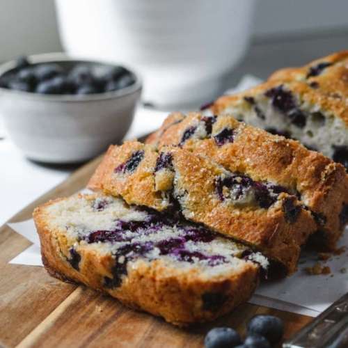Blueberry loaf cake sliced with slices layered onto of each other. A bowl of blueberries next to it.