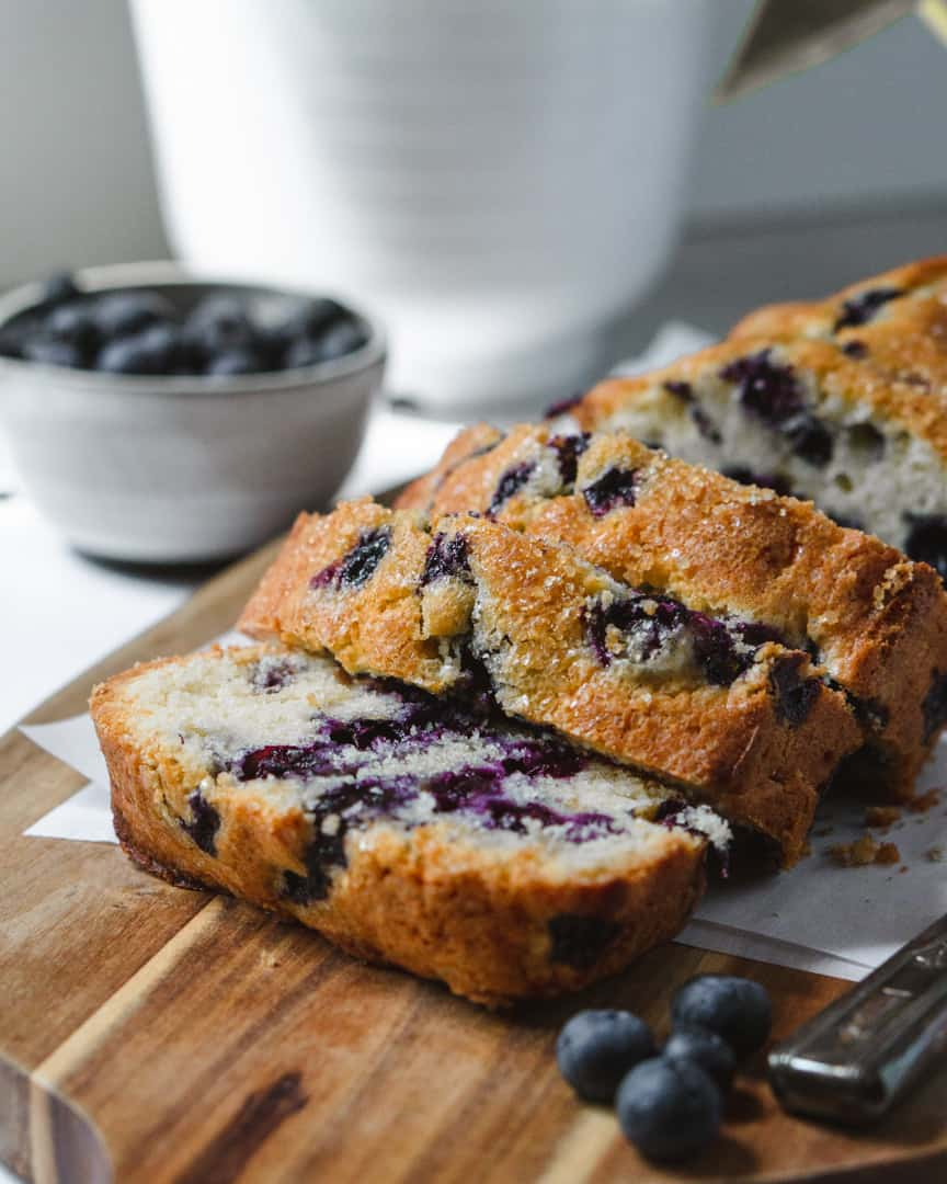 Blueberry loaf cake sliced with slices layered onto of each other. A bowl of blueberries next to it.