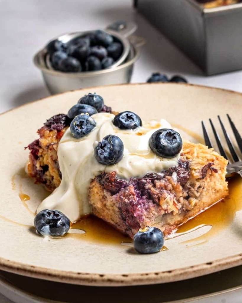 Blueberry baked oatmeal slice with yogurt, maple syrup and fresh blueberries on top.