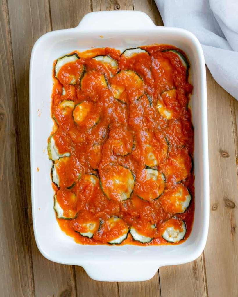 A baking pan with sliced zucchini rounds topped with red sauce.