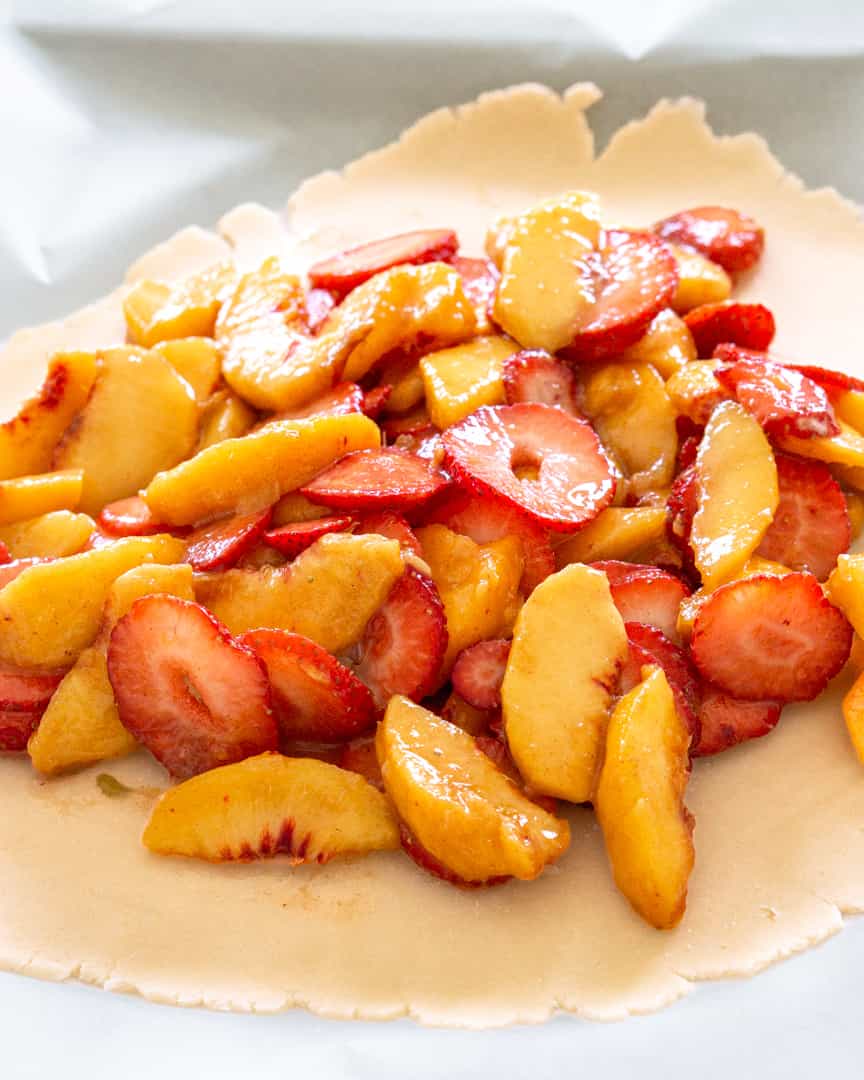 strawberries and peaches piled in the center of a rolled out pie crust.
