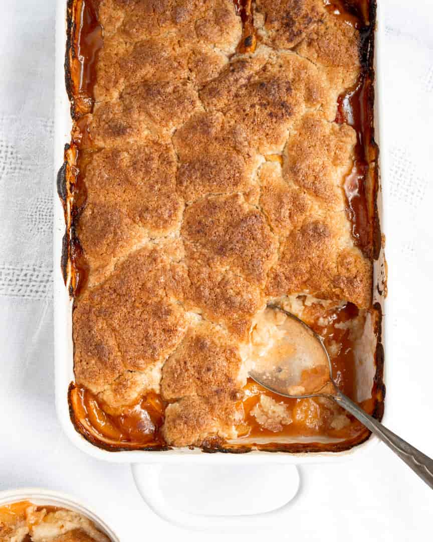 Peach cobbler with a piece scooped out and a spoon in the scooped out space.
