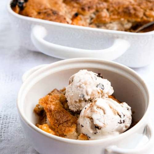 peach cobbler in the background with a small bowl with a scoop of cobbler and two scoops of ice cream on top.