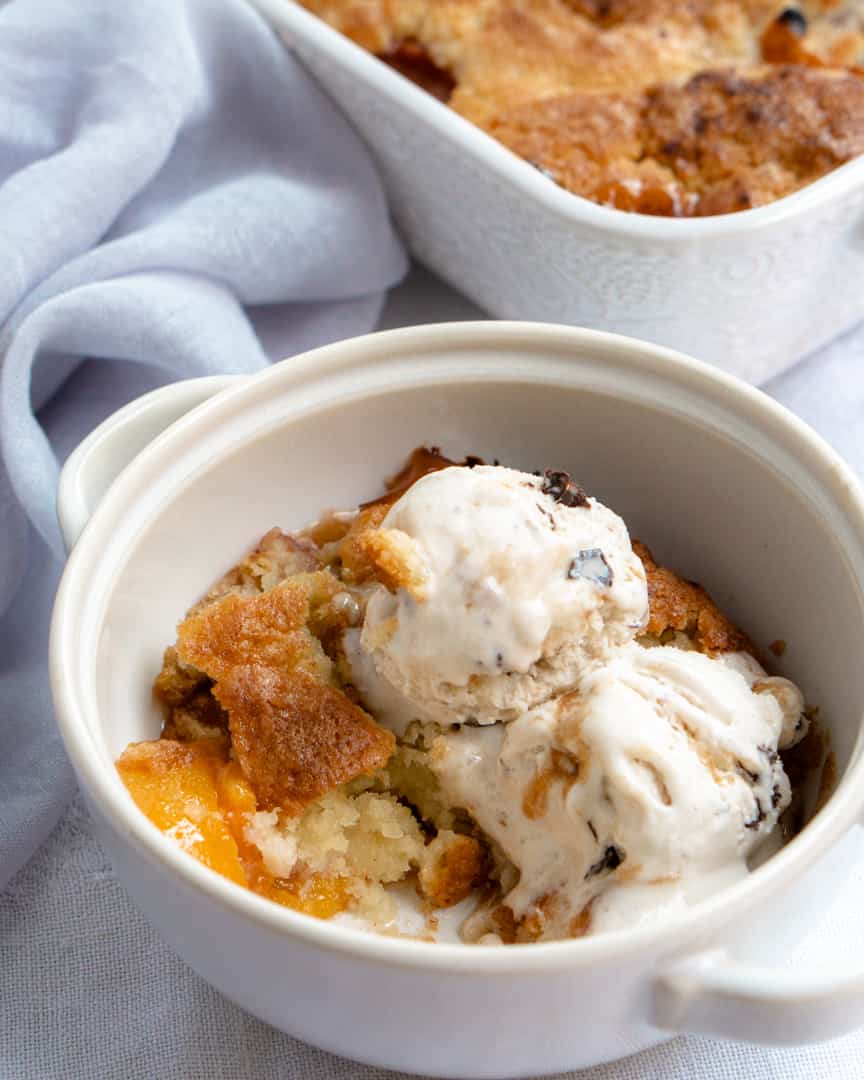 small round bowl with peach cobbler topped with two scoops of ice cream