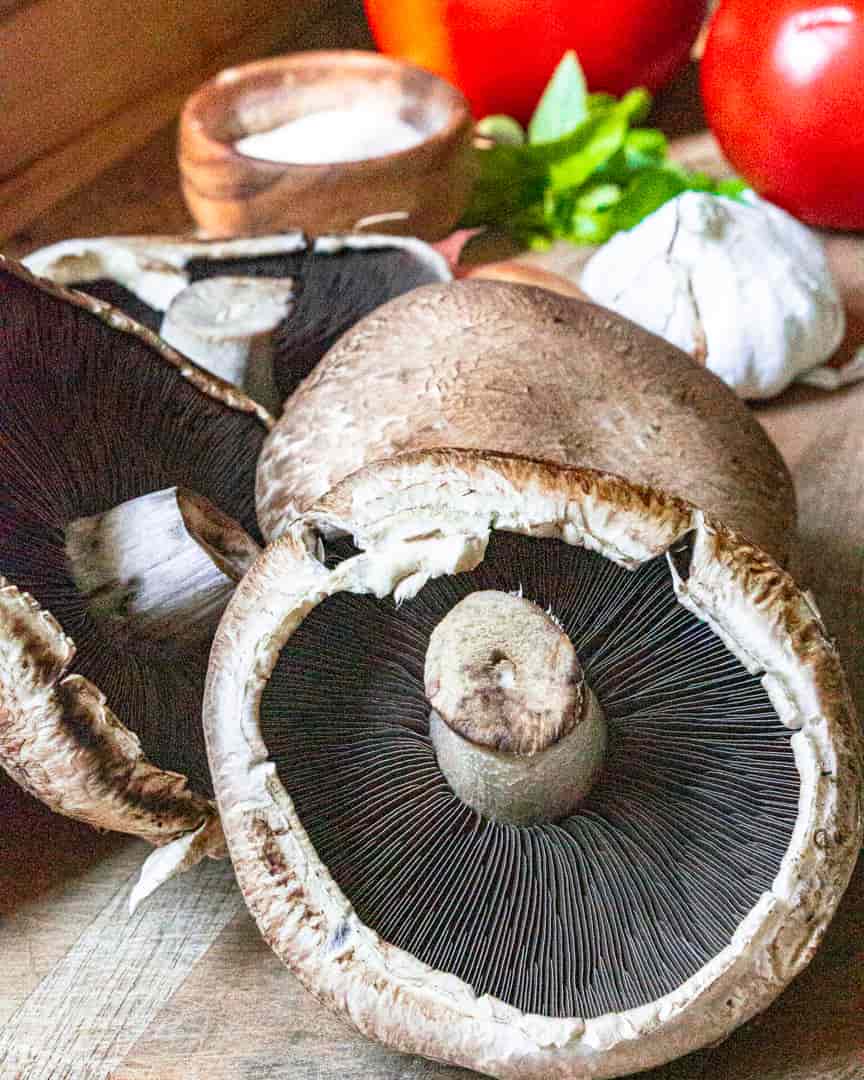 Portobello mushrooms flipped upside down next to garlic bulb, tomatoes and basil