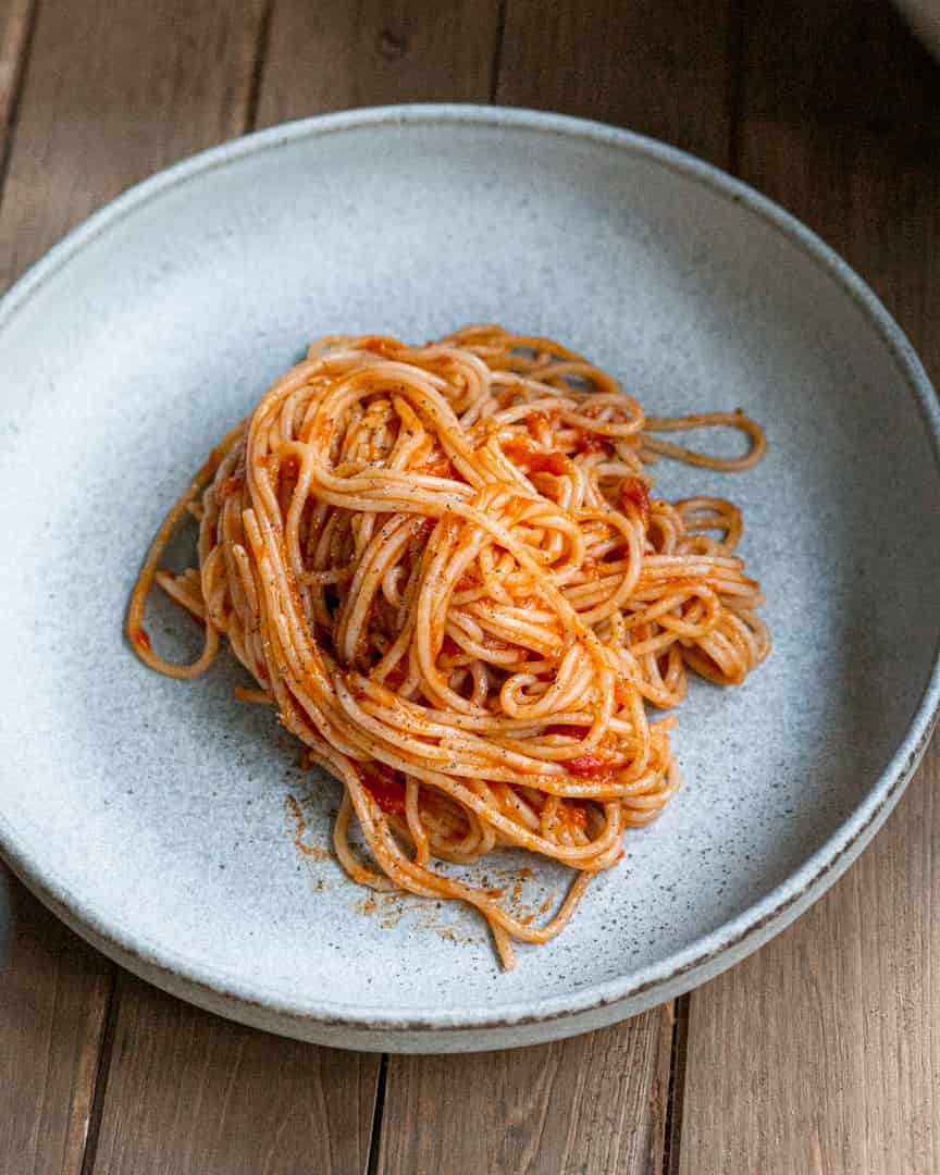 A plate of spaghetti mixed with marinara sauce.