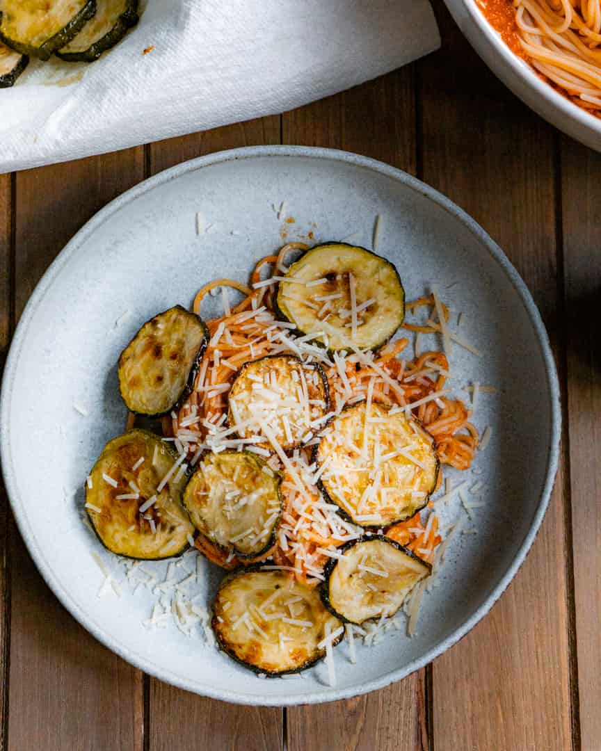 A plate of pasta with zucchini and shredded cheese on top of the pasta.