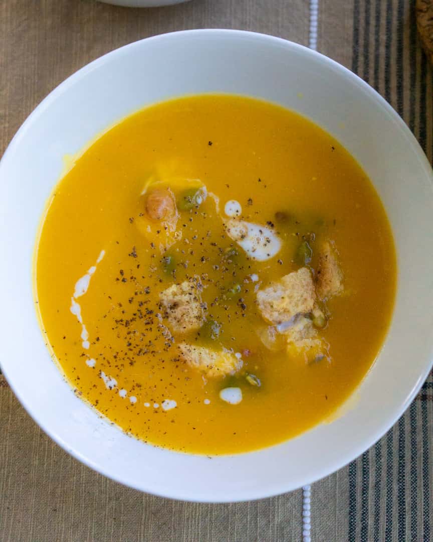 Butternut squash soup with croutons and pumpkin seeds as toppings. A heavy cream drizzle swirled on top.