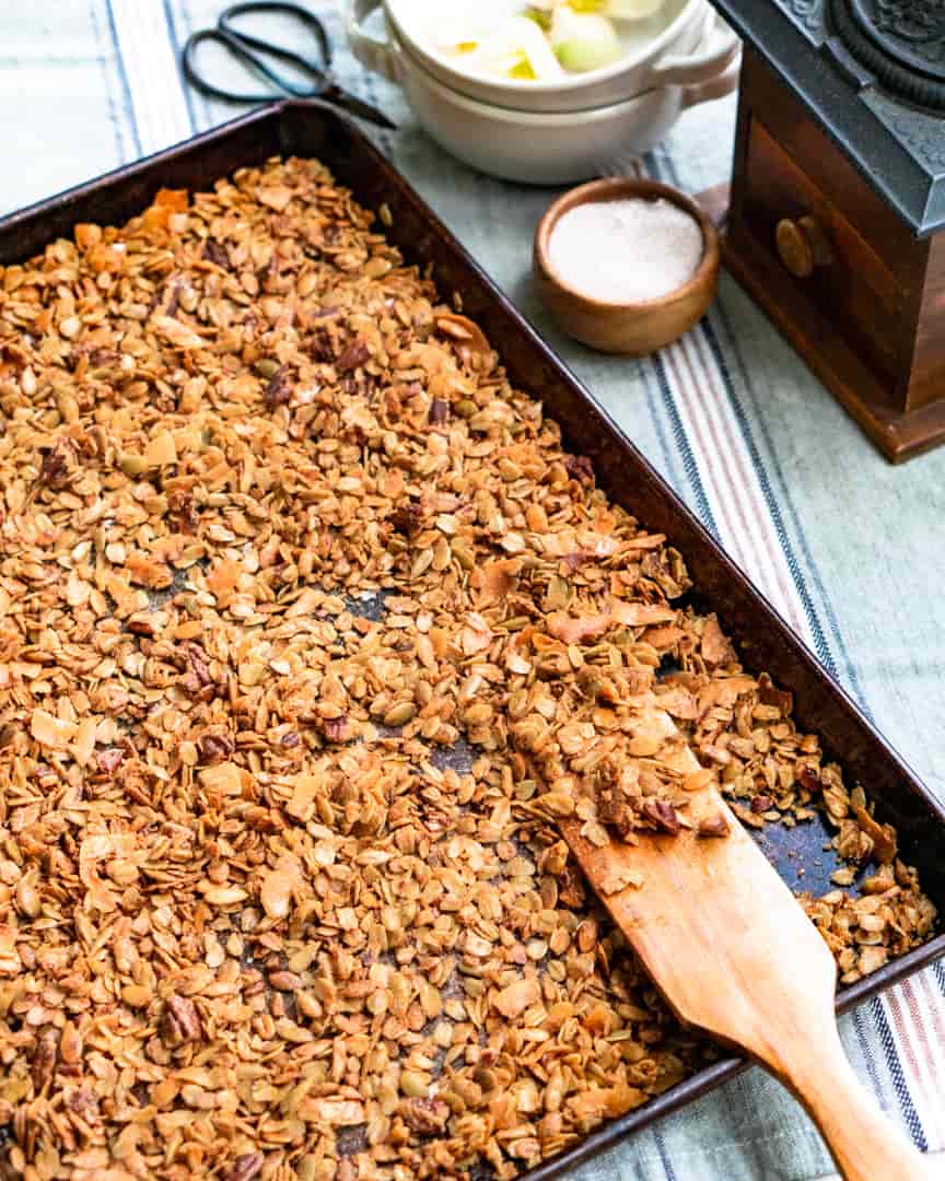 A baking sheet with toasted granola and a wooden spurtle laying in the granola