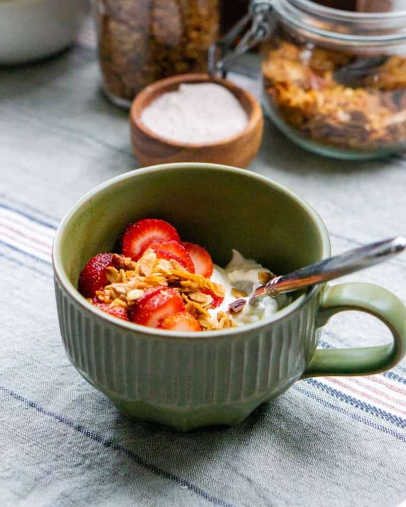 A mug of yogurt topped with sliced strawberries and granola sprinkled on top.