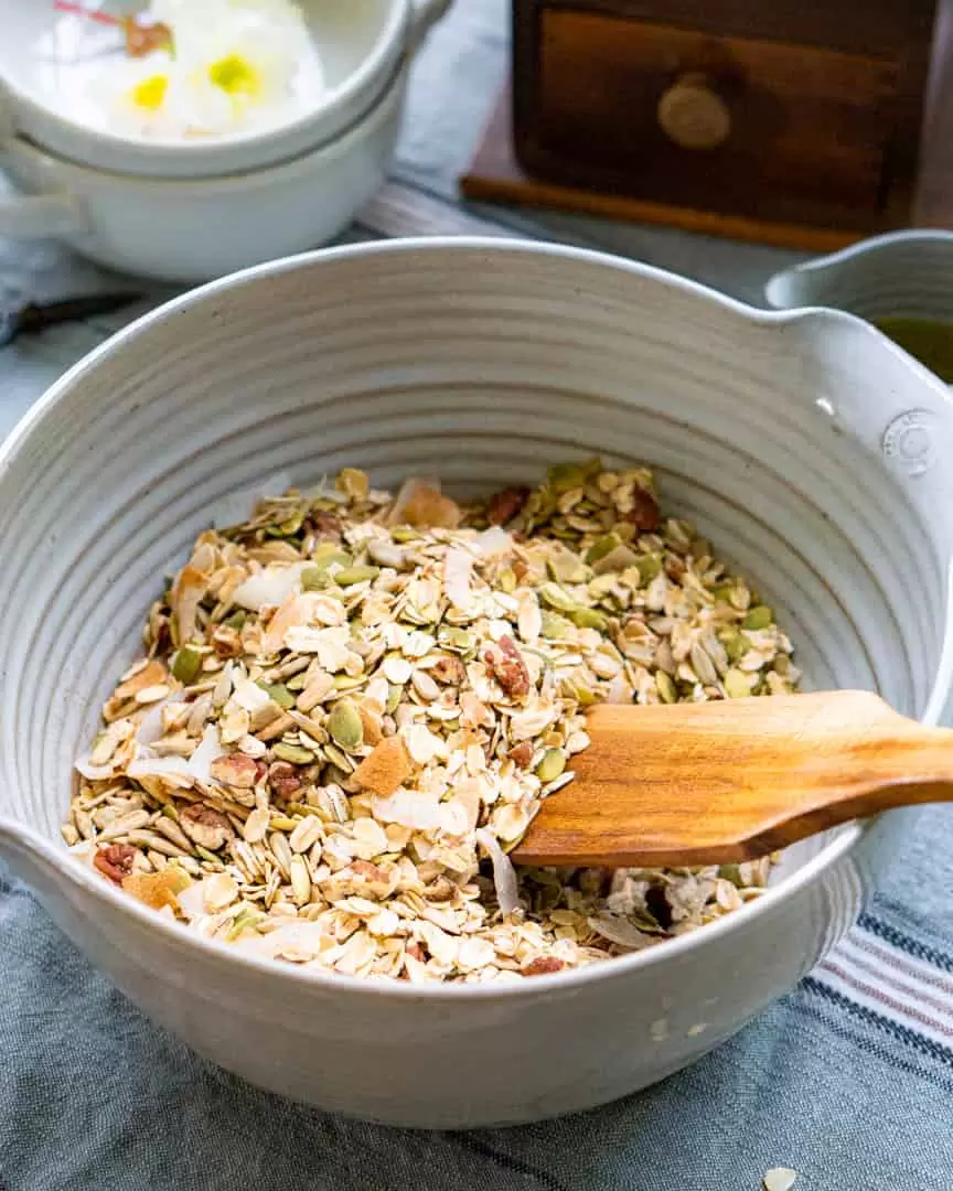 Raw granola in a bowl with a wooden spurtle.