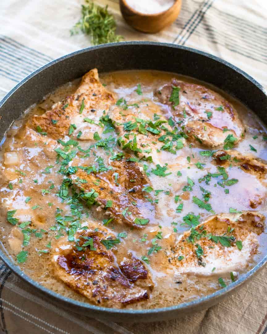A skillet with pork chops in a pan sauce sprinkled with fresh parsley.