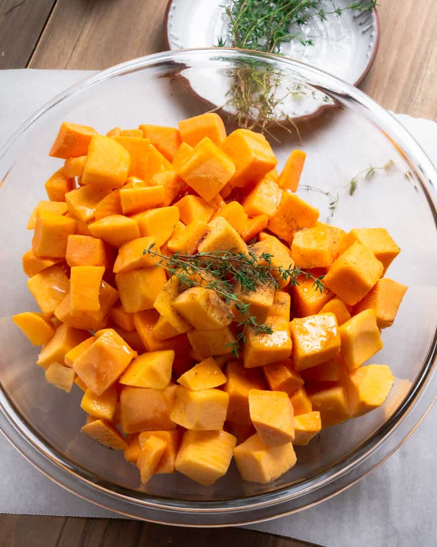 Cubbed butternut squash in a bowl with fresh thyme sprigs on top