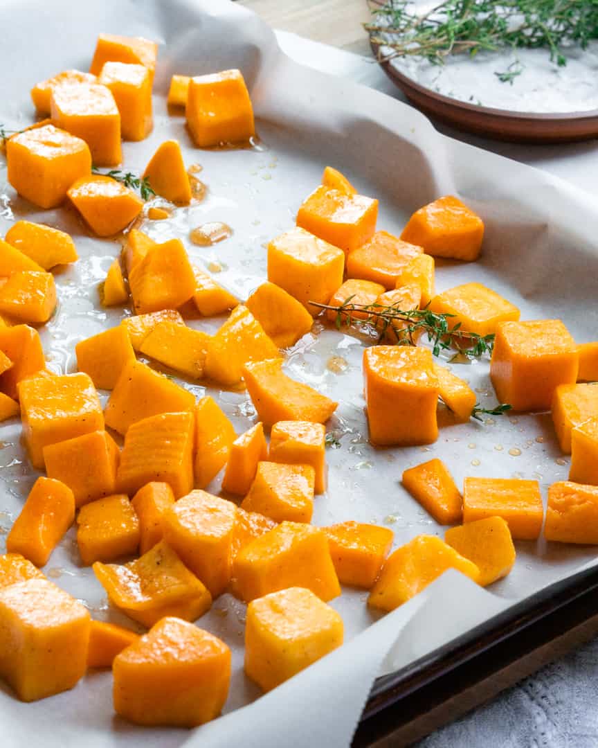 Cubes of butternut squash on a baking sheet with fresh thyme sprigs.