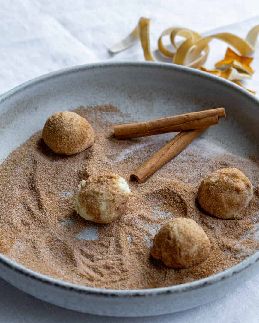 Raw cookie dough balls on a plate with cinnamon sugar.