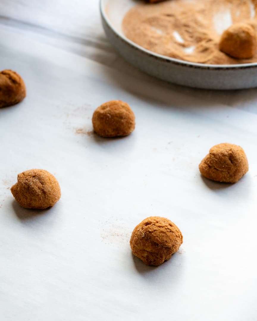 Cookie dough balls covered in cinnamon sugar on a baking sheet.