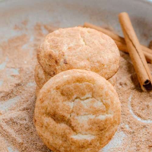 Snickerdoodle Cookies on a bed of cinnamon sugar with cinnamon sticks next to it.