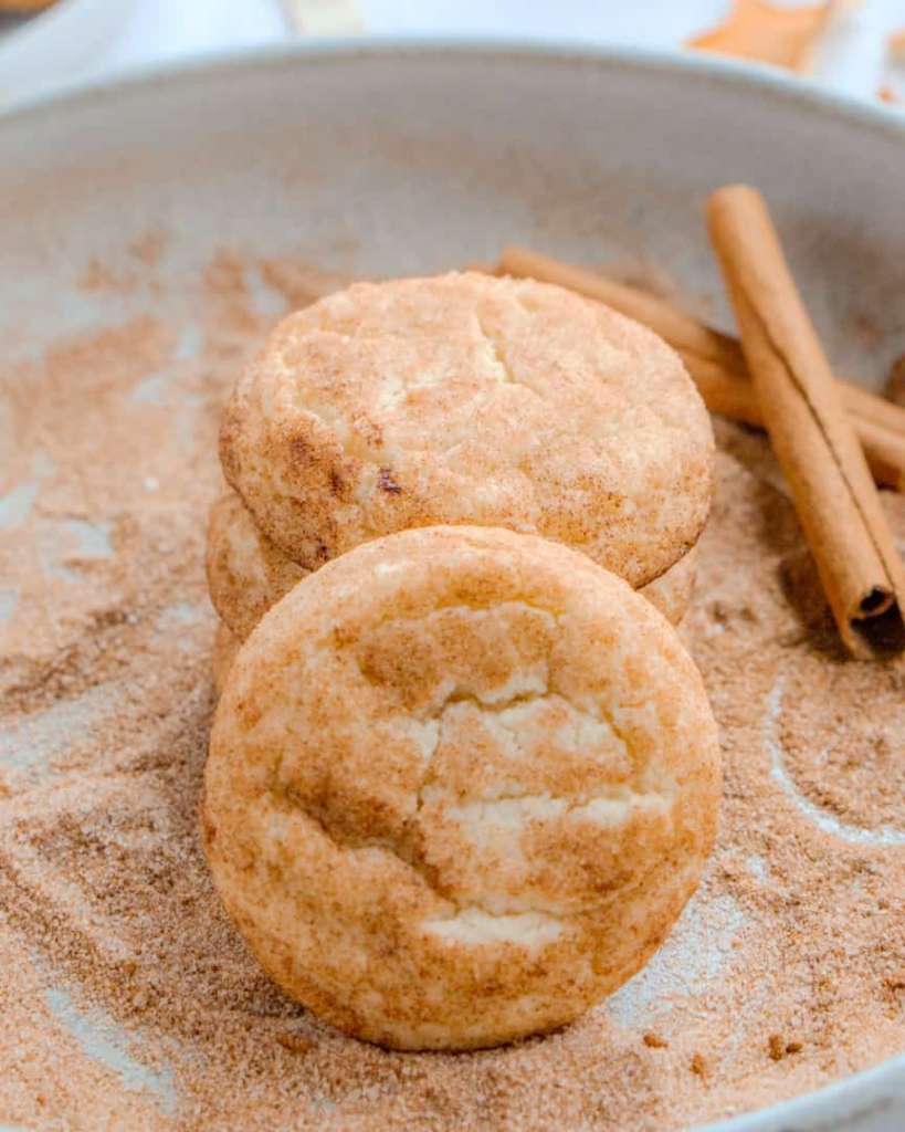Snickerdoodle Cookies on a bed of cinnamon sugar with cinnamon sticks next to it.