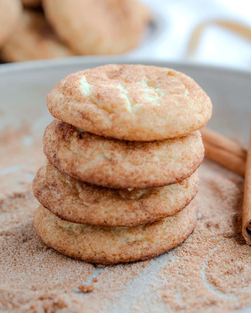 Snickerdoodle cookies stacked on top of each other on a plate covered in cinnamon sugar.