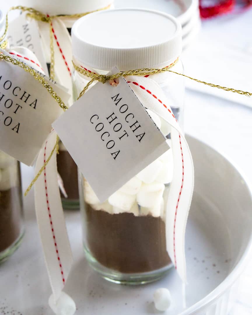 A tall jar filled with hot cocoa mix and marshmallows. Tied with a ribbon and a label and directions attached. The label says Mocha hot cocoa.